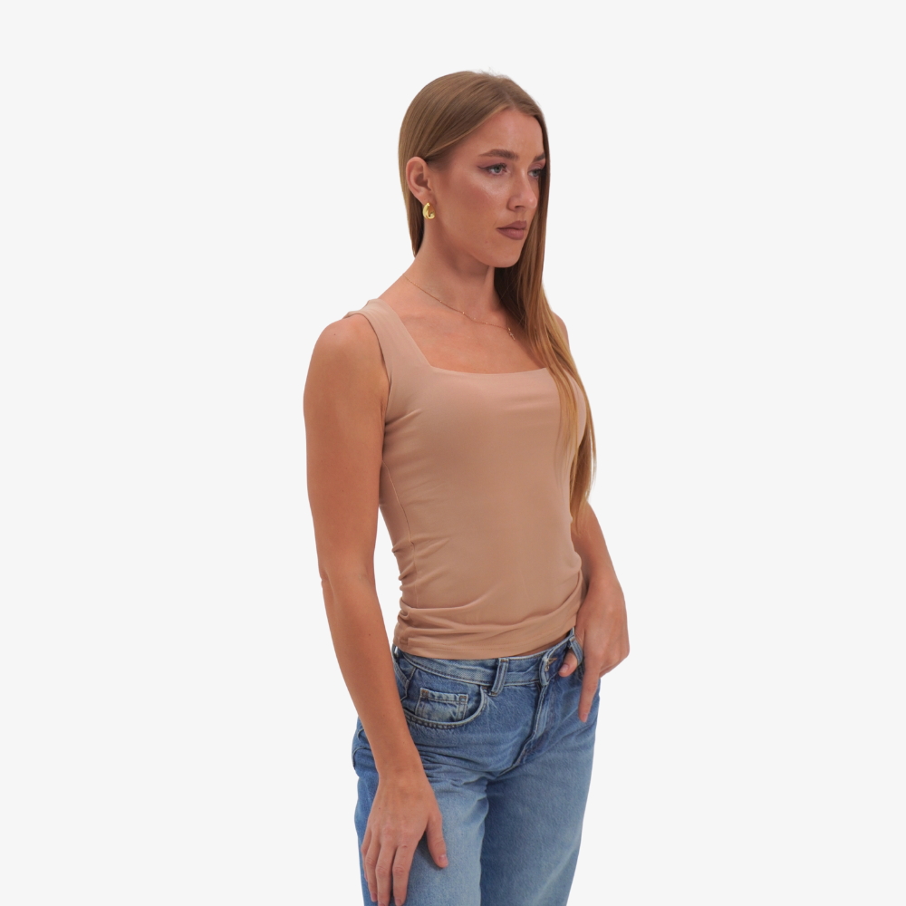 Charlotte top Woman wearing a beige tank top and blue jeans on a white background